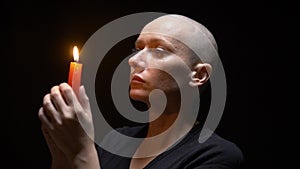 Portrait of a bald woman with a candle on a black background. copy space