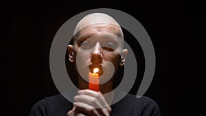 Portrait of a bald woman with a candle on a black background. copy space