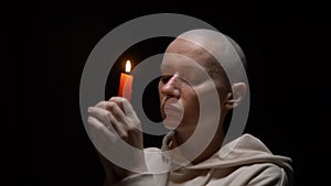 Portrait of a bald woman with a candle on a black background. copy space