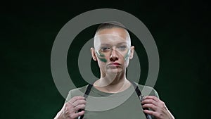Portrait of a bald woman in military camouflage makeup and harness looking at the camera and posing. copy space