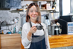 Portrait of barista woman or coffee maker hold a cup and stand in front of counter in coffee shop with looking at camera and smile
