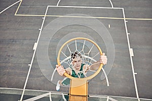 Portrait of basketball player hanging on net on a basketball court. Young man playing basketball outside doing slam dunk