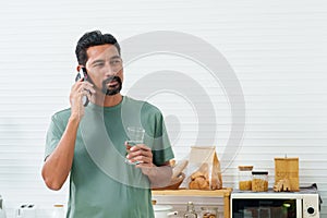 Portrait, Bearded Asian man wearing t-shirt on casual day. Standing in the kitchen talking on the mobile phone while waiting to