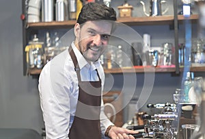 Portrait of bearded barista in apron smiling at camera and preparing coffee at counter. Small business owner concept