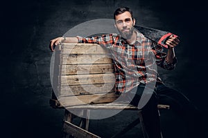 Portrait of bearded carpenter male holds handsaw on a shoulder.