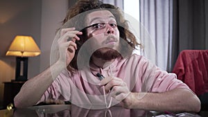 Portrait of bearded Caucasian man with brown eyes and long curly hair looking at camera and applying mascara. Intersex