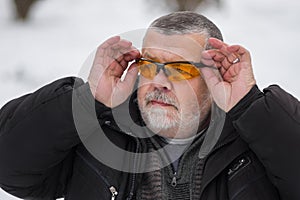 Portrait of bearded Caucasian senior man adjusting sun glasses at winter season