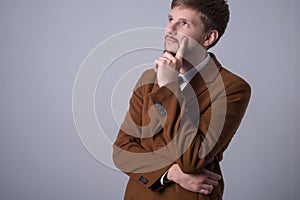 Portrait of a bearded dreaming man holding his hand near the chin, dreams looking up. On a gray background