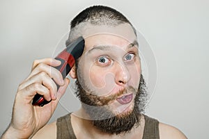 Portrait of a bearded guy cuts his beard, hair on his head and mustache with a clipper on an isolated background