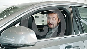 Portrait of bearded guy new car owner sitting inside beautiful automobile smiling