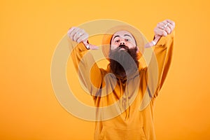 Portrait of bearded hipster with hat showing thumb down sign over yellow background
