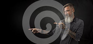 Portrait of a bearded hipster, who is pointing with his fingers to something, isolated on a black background