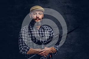 Portrait of a bearded hunter traveler in a fleece shirt and hat holds rifle with a sight and binoculars.