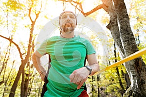Portrait of a bearded man in age stands near a taut slackline in an autumn forest