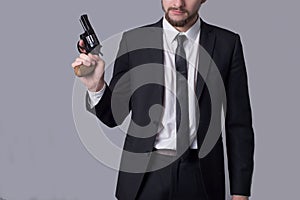 Portrait of a bearded man in a business suit holding a revolver. On a gray background
