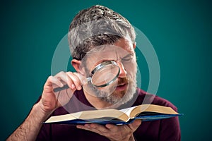 A portrait of bearded man holding opened book and magnifying glass. People, education and searching concept