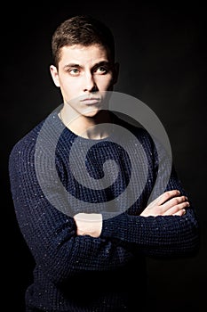 Portrait of a bearded man with an intense look standing in a dark room against a black background.