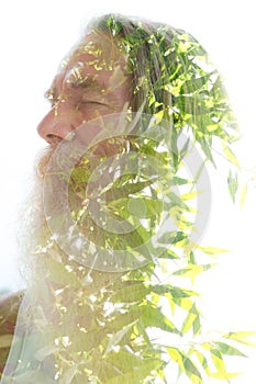 A portrait of a bearded man merging into young tree leaves in a double exposure