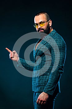 Portrait of bearded man with pointing finger at copyspace  over dark blue background. Guy in sunglasses pick on