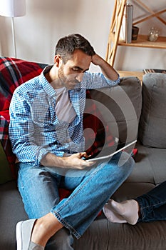 Portrait of bearded man sitting at home, indoors and using digital tablet. Concept of family, love, relationship