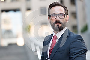 Portrait of bearded man in suit on background of building. Handsome businessman outdoor. Male business person stands on street and