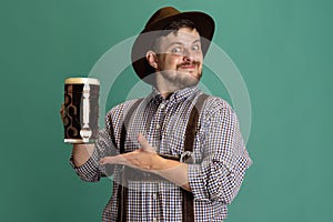 Portrait of bearded man in traditional Bavarian costume with one liter of dark beer isolated over green background