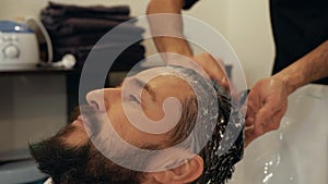 Portrait bearded man washing head with shampoo in barber shop. Male stylist washing hair in barber salon. Male