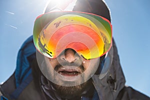 A portrait of a bearded man wearing ski goggles on his way to the top of the mountain. The concept of endurance in the