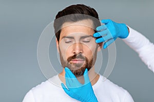 Portrait of bearded middle aged man getting prepared for plastic surgery procedures, doctor touching male face skin