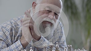 Portrait of bearded old mature man thinking which chess piece to make a move. Two people playing a game of chess sitting