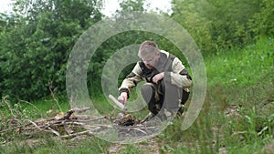 Portrait of bearded skilled fisherman putting brushwood on campfire to making fire on bank of river in evening before