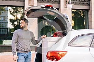 Portrait of bearded young delivery man wearing casual clothing standing near car.