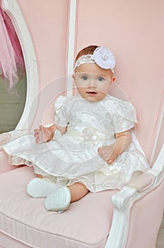 Portrait of Beatiful babygirl in white dress on pink chair in the studio. Cute kids.
