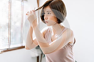 Portrait of beauiful young Asian woman having her hair cut with scissors at home. She`s stay at home during the coronavirus