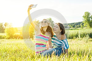 Portrait of beautiful adult mother and her daughter teenage girl making a selfie using smart phone and smiling.