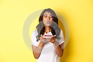 Portrait of beautiful african-american girl celebrating birthday, blowing lit candle on b-day cake and making a wish