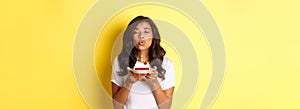 Portrait of beautiful african-american girl celebrating birthday, blowing lit candle on b-day cake and making a wish