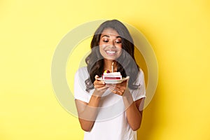 Portrait of beautiful african-american girl celebrating birthday, smiling and looking happy at b-day cake with candle