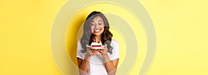 Portrait of beautiful african-american girl celebrating birthday, smiling and looking happy at b-day cake with candle