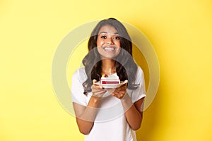 Portrait of beautiful african-american girl celebrating birthday, smiling and looking happy and holding b-day cake with