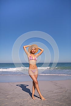 Beautiful woman in bikini and hat looking at camera on beach in the sunshine