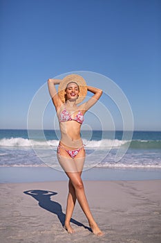 Beautiful woman in bikini and hat looking at camera on beach in the sunshine