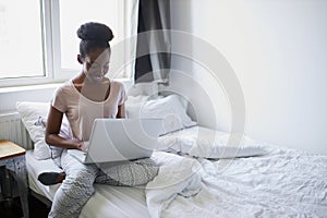 Portrait of beautiful african lady on bed with laptop