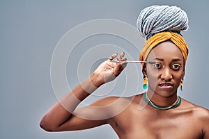 Portrait of beautiful Afro American girl holding a mascara and looking at camera, on a grey background