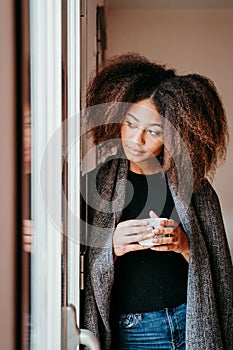 portrait of beautiful afro american young woman by the window holding a cup of coffee. Lifestyle indoors