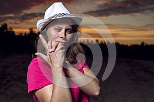 Portrait of beautiful American girl in cowboy hat folded her arms with gun against beautiful sky at sunset
