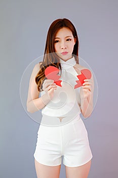 Portrait beautiful asia woman on gray background, unhappy in valentine day concept, model is holding red half heart in hand, broke