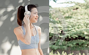 Portrait Beautiful Asian adult sportive woman wearing sport bra, resting, putting headphone to listen music with happiness and