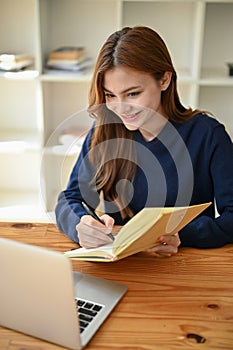 A portrait of a beautiful Asian female college student making notes on her book