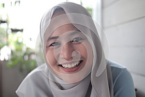 Portrait of beautiful Asian muslim woman smiling at camera, woman stiting relaxing outside her home